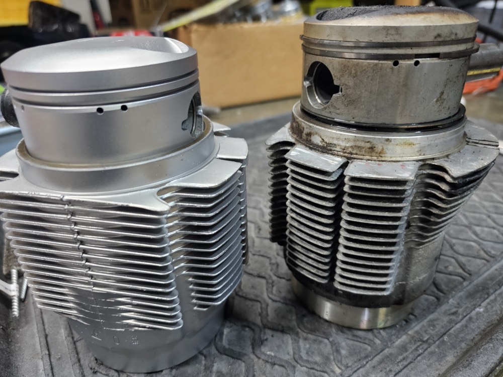 Two motorcycle cylinder jugs side by side, the left one vapor honed to bare aluminum and the right still carbon caked