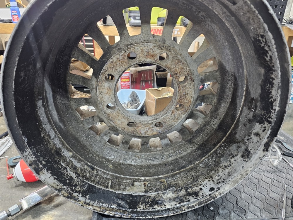 Truck wheel before restoration, coated in baked on grime with surface rust around the lug holes